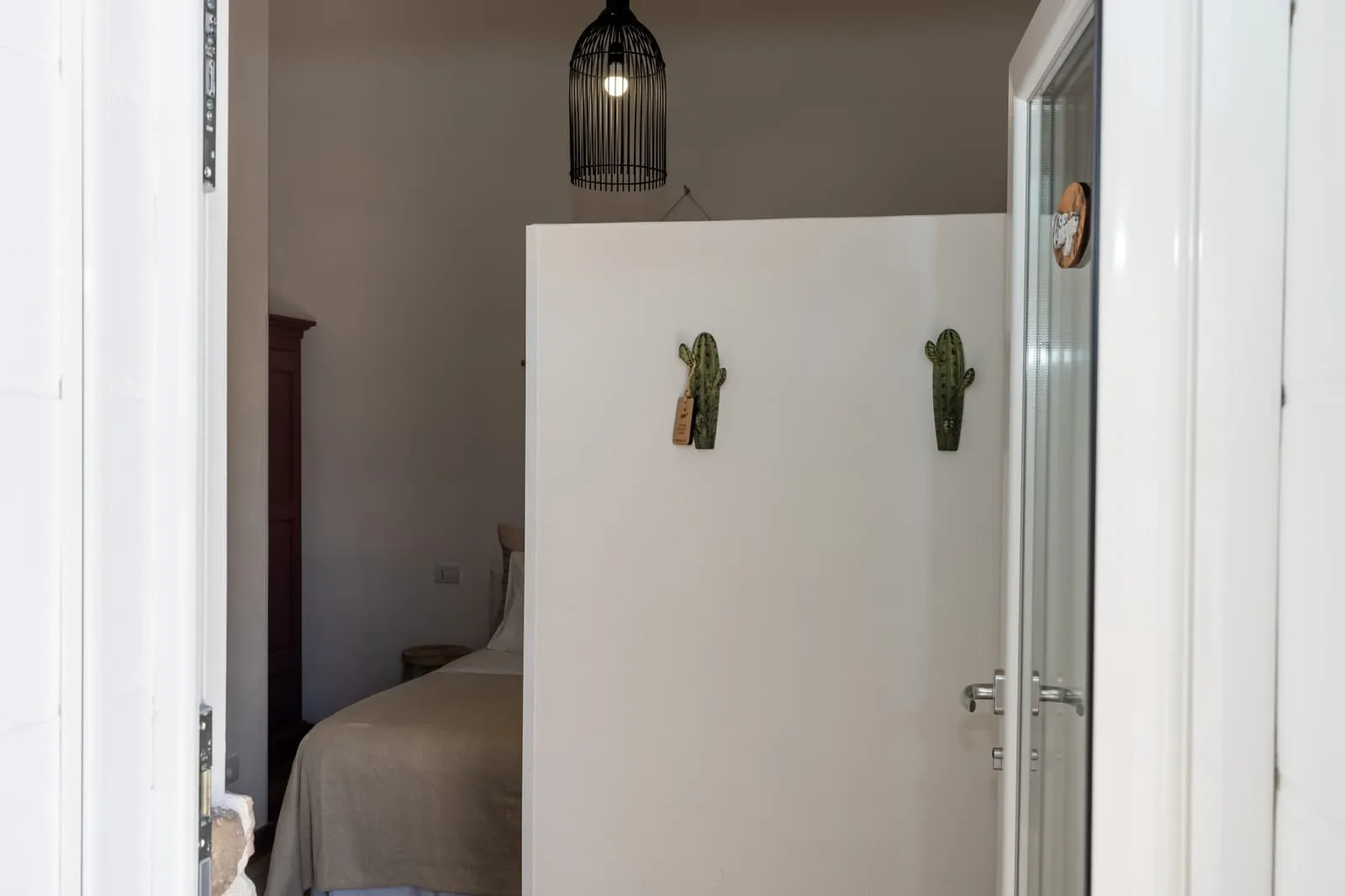 Ingresso della camera Ciliegio con lampada in vimini e letto sullo sfondo
