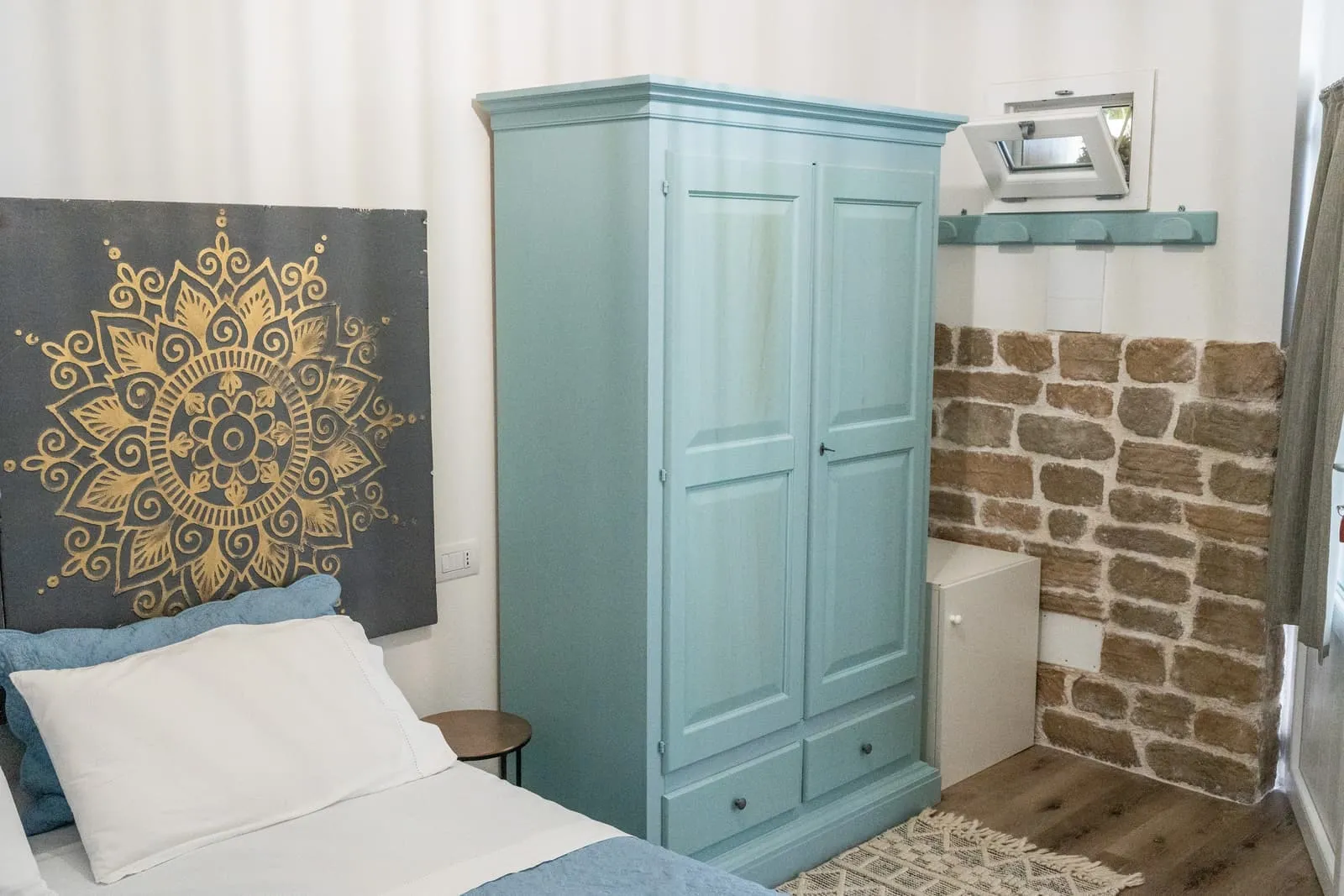 Camera Melograno con armadio azzurro dipinto, testiera mandala e muro in pietra